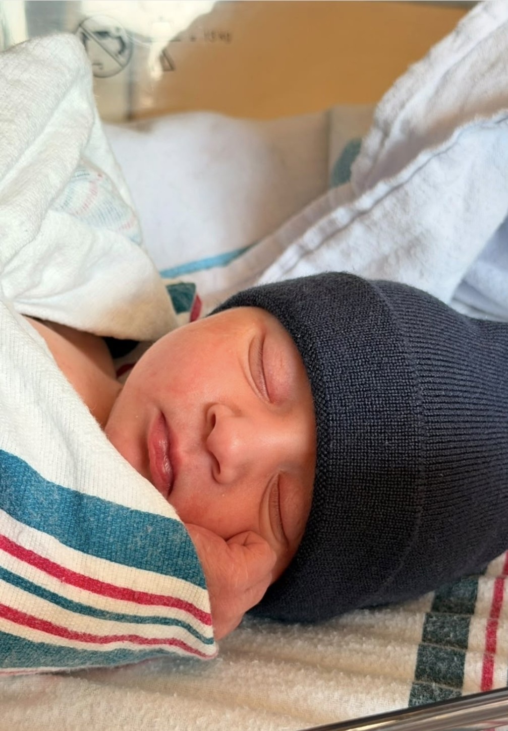 A newborn sleeping peacefully in a dark knit hat