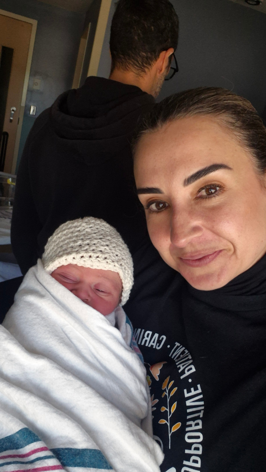 A doula holding a swaddled newborn in a knitted cream hat