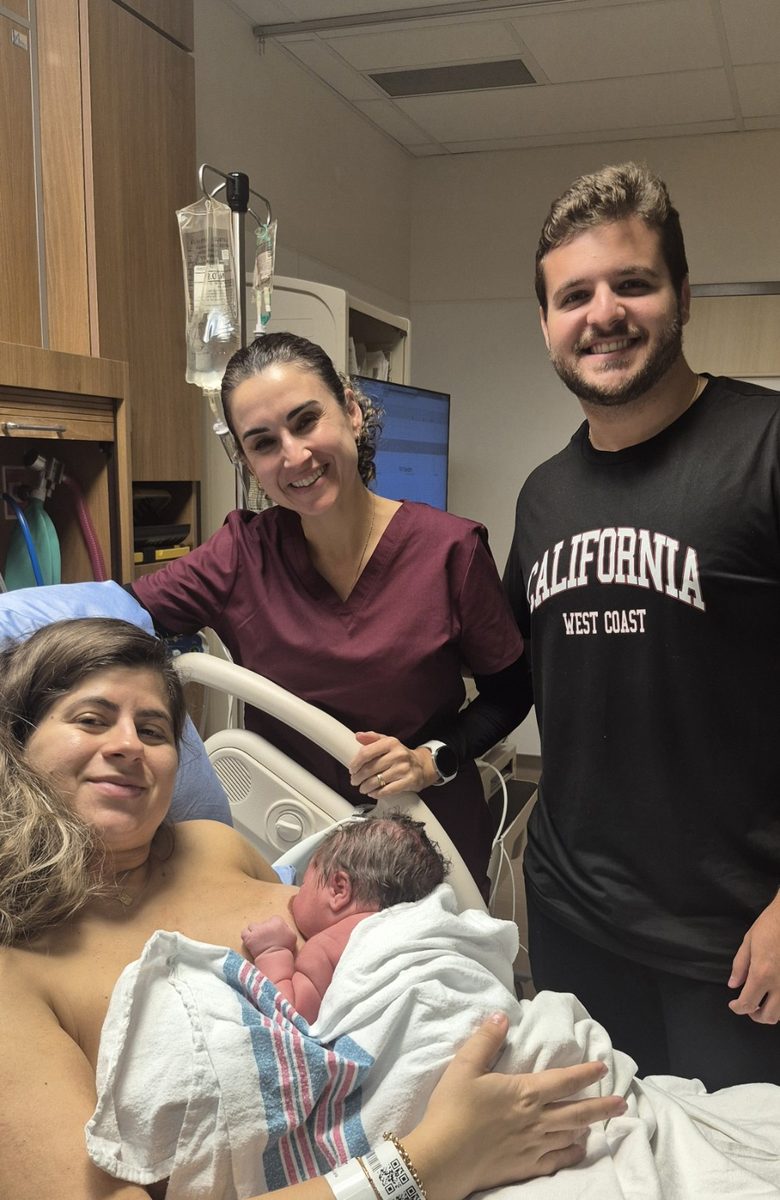 A family smiling with their doula as they hold their newborn in hospital