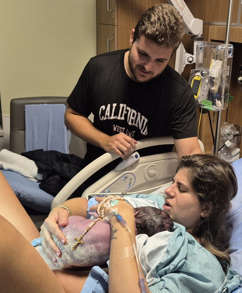 A birthing parent cradling their newborn skin-to-skin right after birth, with their partner close by