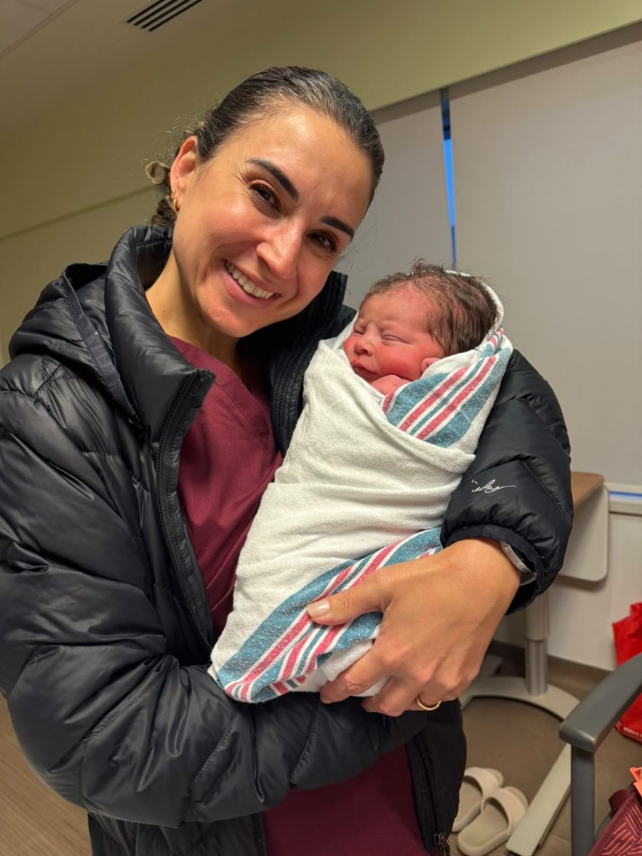 Camila smiling as she holds a newborn wrapped in a striped blanket
